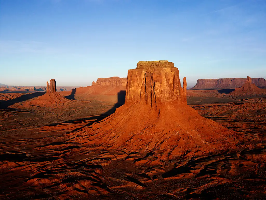 A sandstone butte in Monument Valley at sunset, lit red against a pale sky