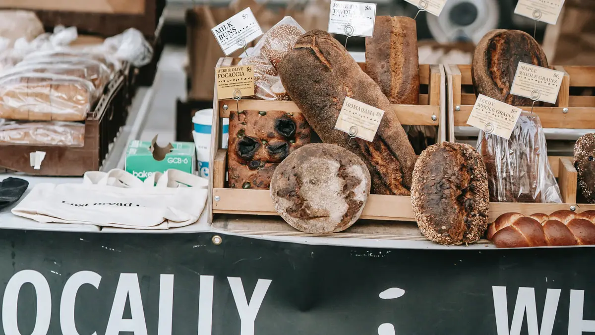 Loaves of bread on a market stall behind a painted sign reading locally