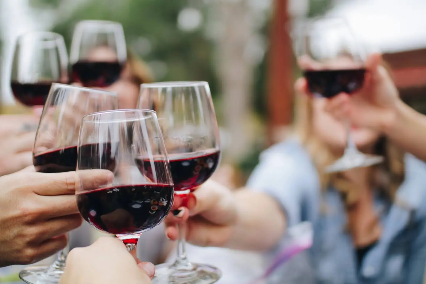 Several hands raising glasses of red wine in a toast outdoors