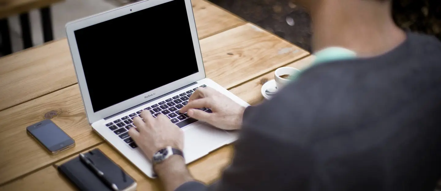 Someone typing on a laptop at an outdoor wooden table